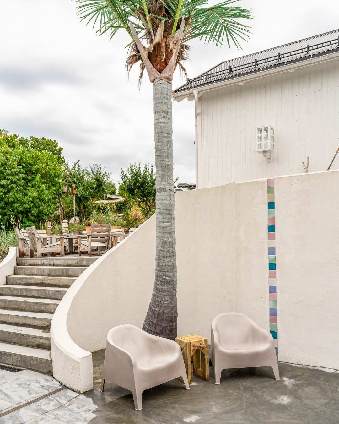 Utvendig støpt murtrapp med kunstig palme og hvitmalt vegg med trekledning. 