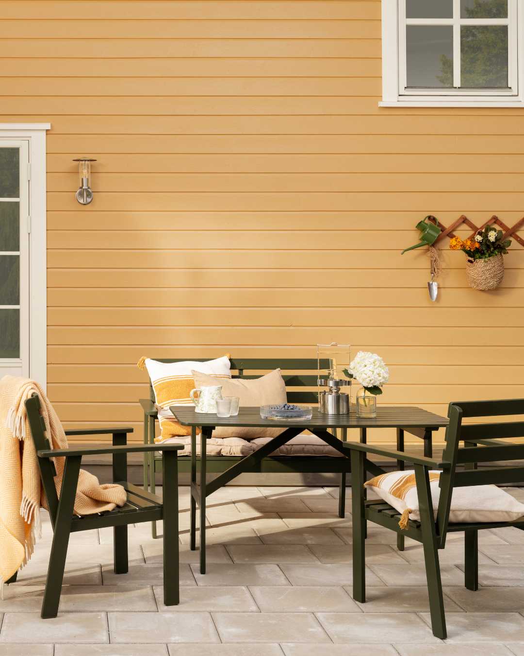 Uteplass med gult hus med liggende trekledning i bakgrunnen