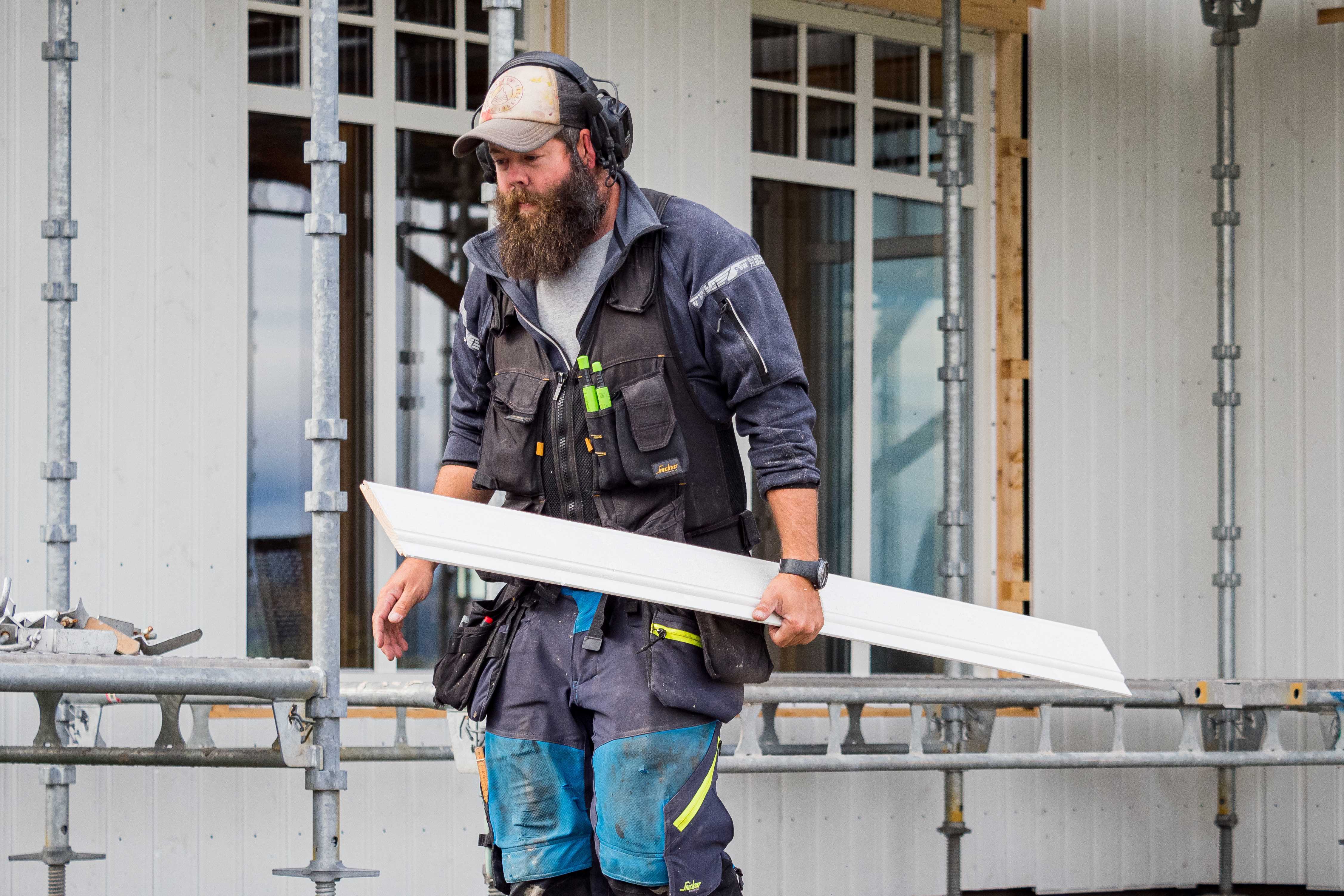 Snekker som bærer et klednignsbord foran huset som er i ferd med å bli kledd.
