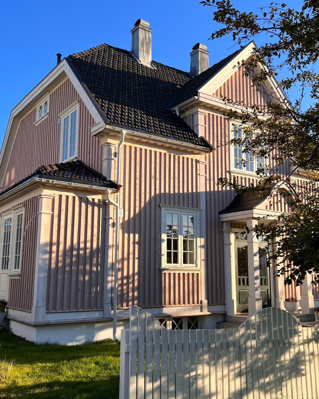 Sidefasade av trevilla med rosa Heftig PRO kledning og hvite vinduskarmer i kveldslys