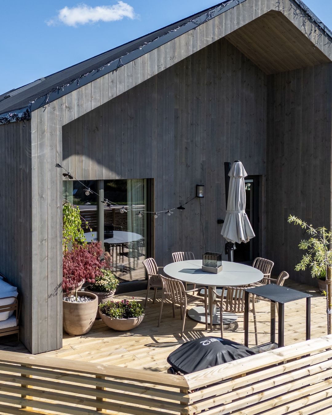 Skjermet uteplass med stående Værbitt kledning i fargen Gråna og lys treterrasse.