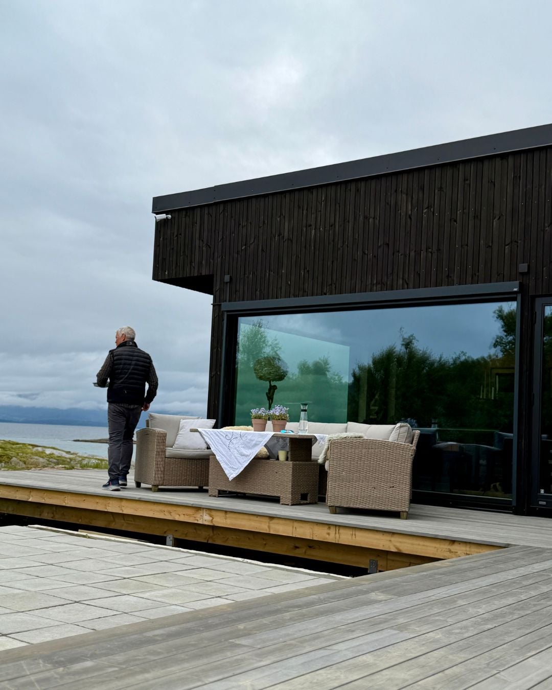 Terrasse ved sjøen foran et moderne hus med mørk Værbitt kledning i fargen Garva.
