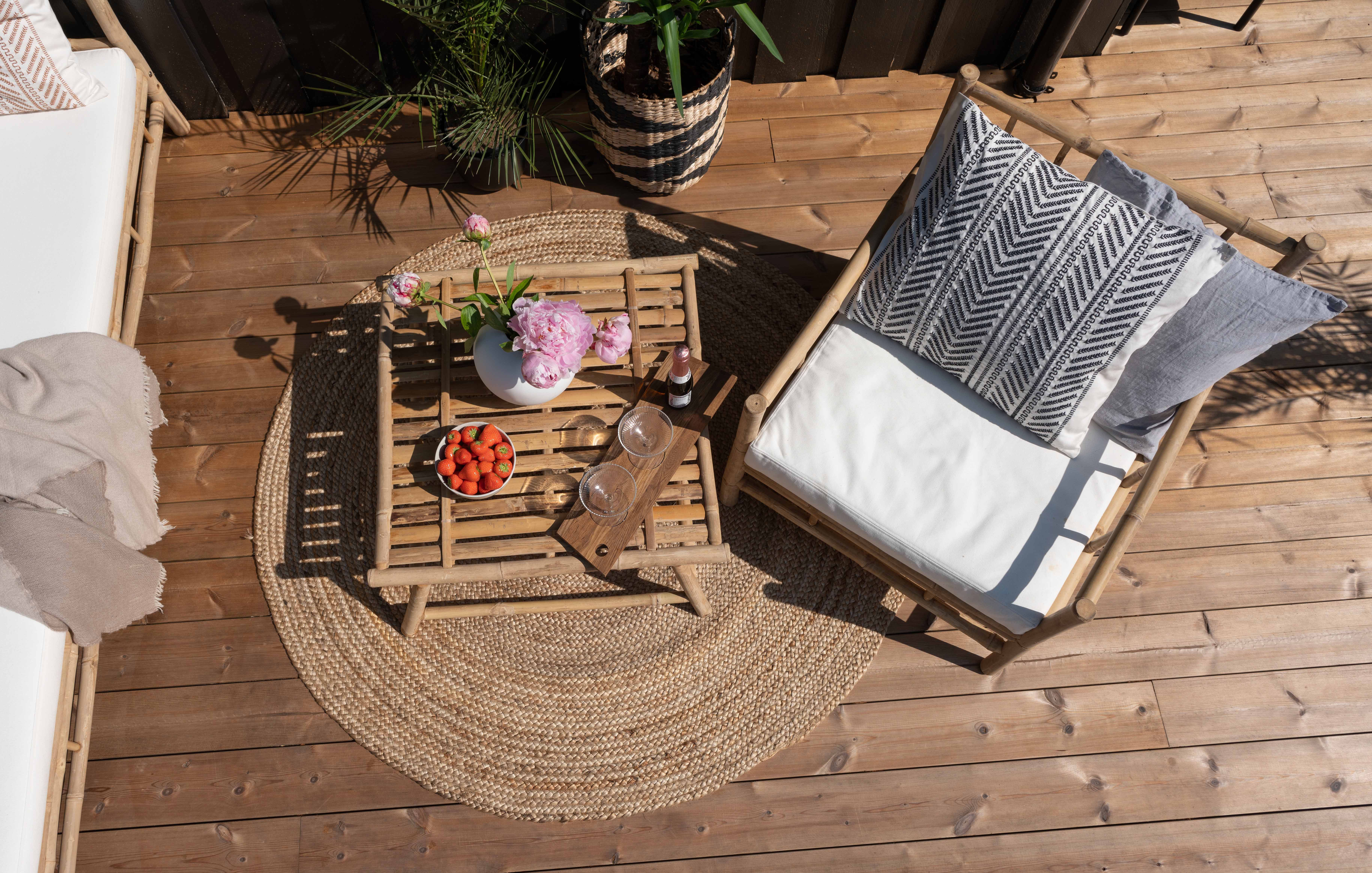 Terrasse med rundt teppe og bali inspirert bambusstol med pute i.