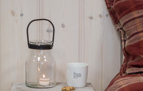 Trepanel Østerdalspanel i hvitlasert på soverom med rødrutete sengetøy, med lykt og kaffekopp på sovebordet